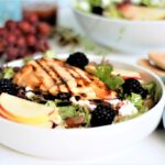 A salad bowl with grilled chicken, blackberries, sliced apples and goat cheese.