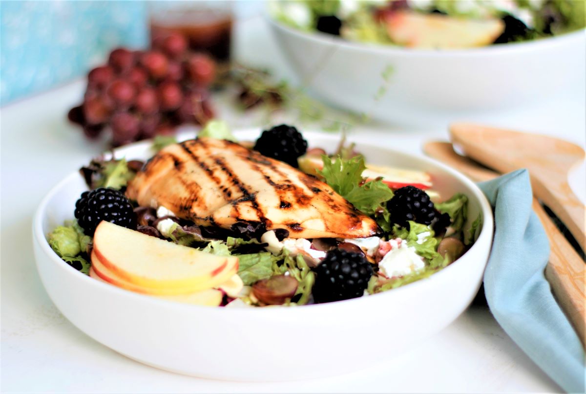 A salad bowl with grilled chicken, blackberries, sliced apples and goat cheese. 