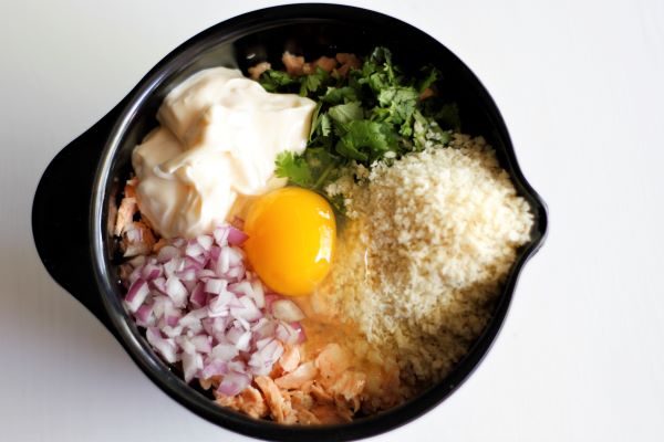 A bowl with ingredients to make salmon cakes, egg, panko crumbs, cilantro, mayonaise, and red onion