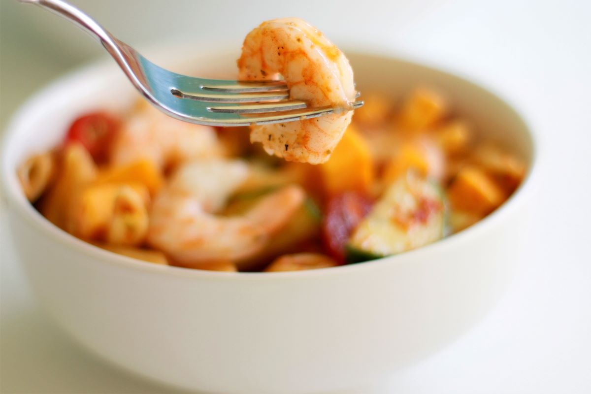 A bowl with shrimp pasta salad and a fork with a shrimp