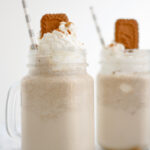 Two milkshakes with topped with whipped cream and a biscoff cookie