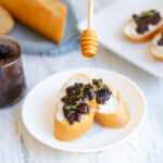 fig compote and goat cheese crostini on a serving platter with honey and a fresh bagguette
