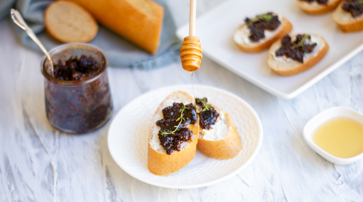 fig compote and goat cheese crostini on a serving platter with honey and a fresh bagguette