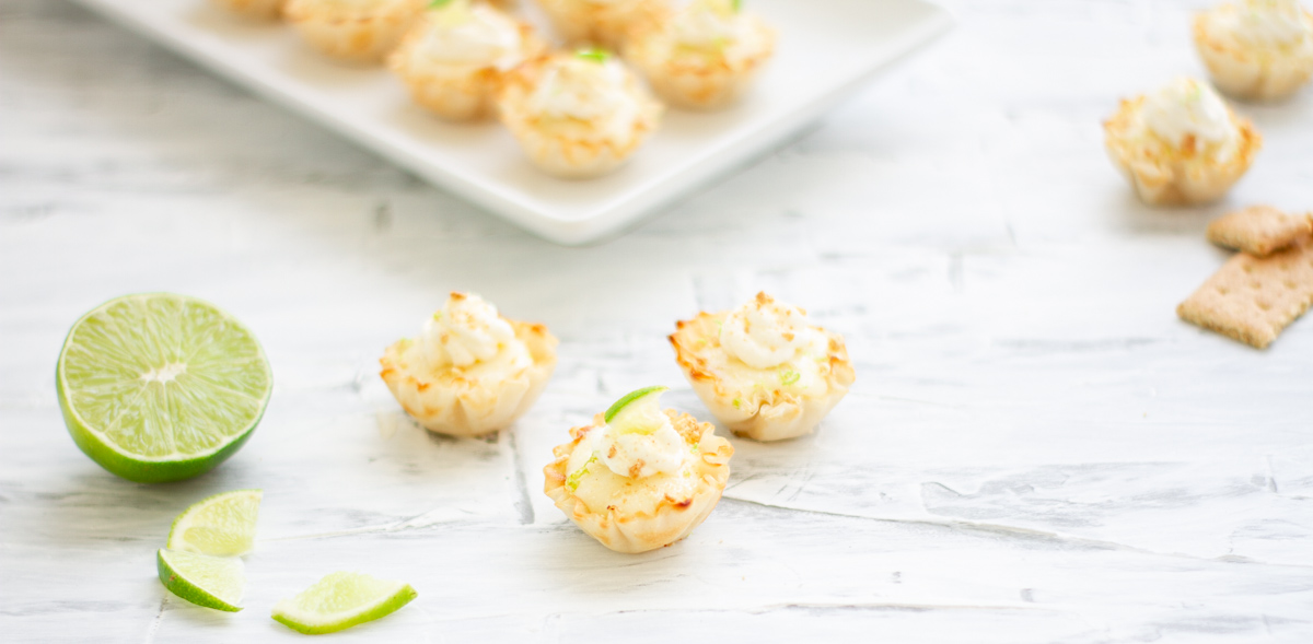 Mini key lime pie bites being decorated with lime wedges and graham cracker crumbs 