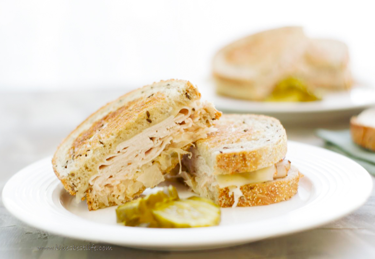 A turkey reuben sandwich on a plate with pickles
