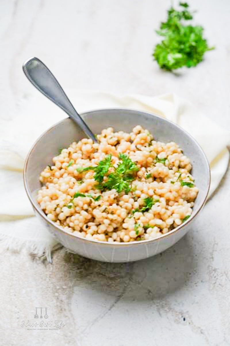 Pearl couscous in a serving bowl garnished with parsley.
