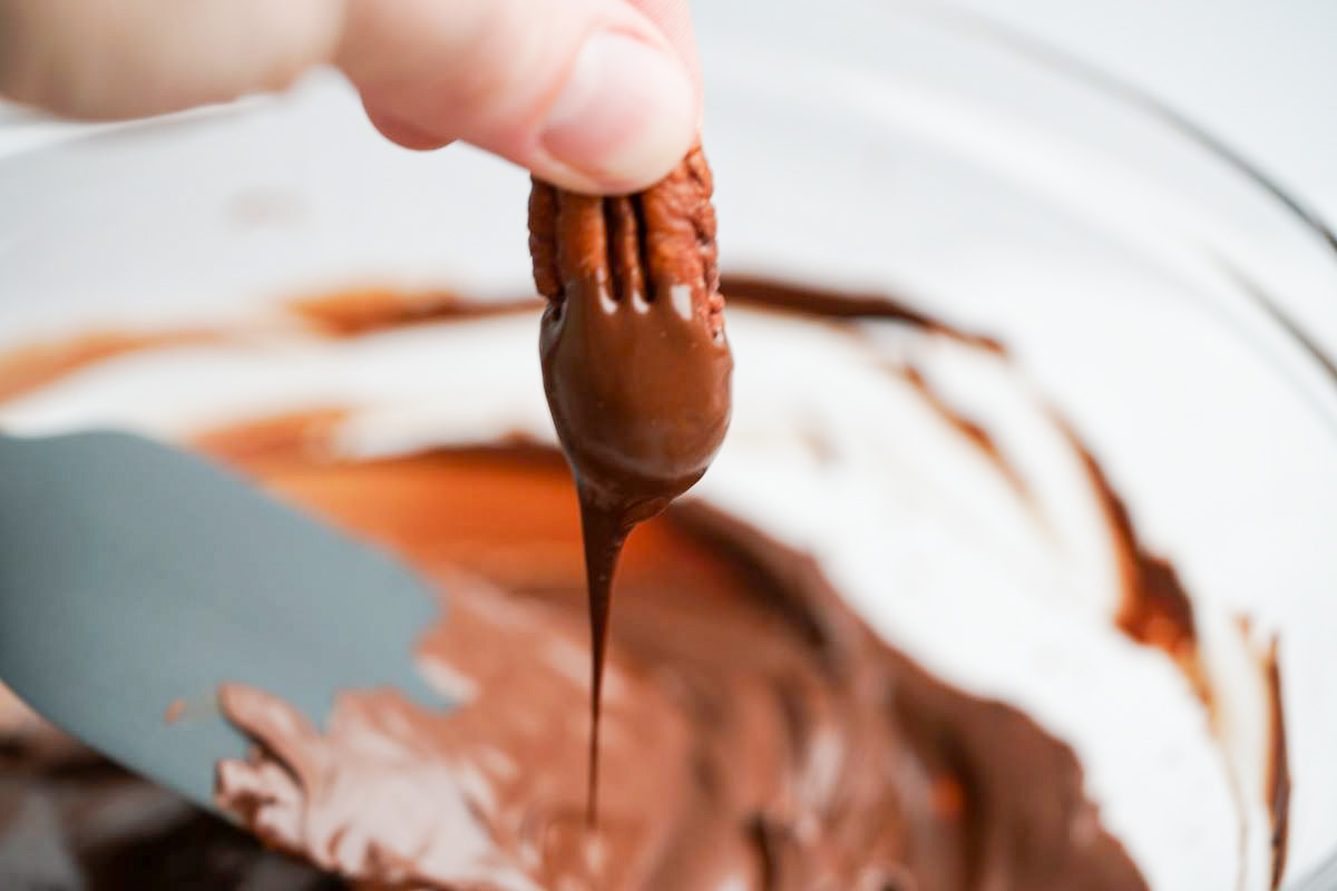 A pecan being dipped in chocolate 