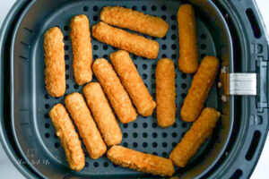 frozen mozzarella sticks in an air fryer basket in a single layer