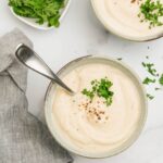 Two bowls of roasted cauliflower soup garnished with parsley and black pepper.