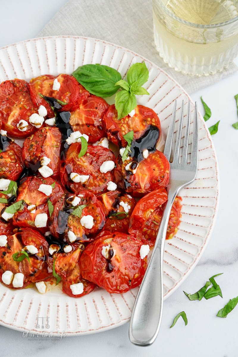 A plate of roasted tomatoes drizzled with balsamic vinegar, basil and goat cheese. 
