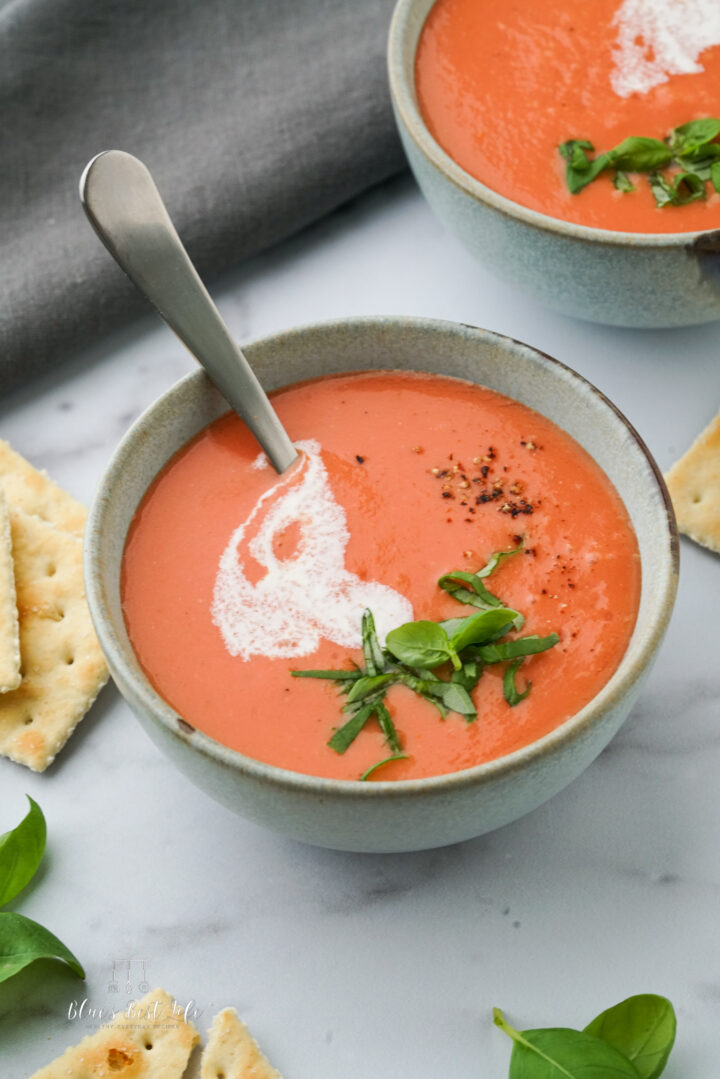 Bowls of tomato soup with heavy cream drizzled over top, fresh basil, and cracked black pepper.  