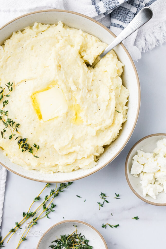 A bowl with mashed potato and cauliflower with thyme and goat cheese.  