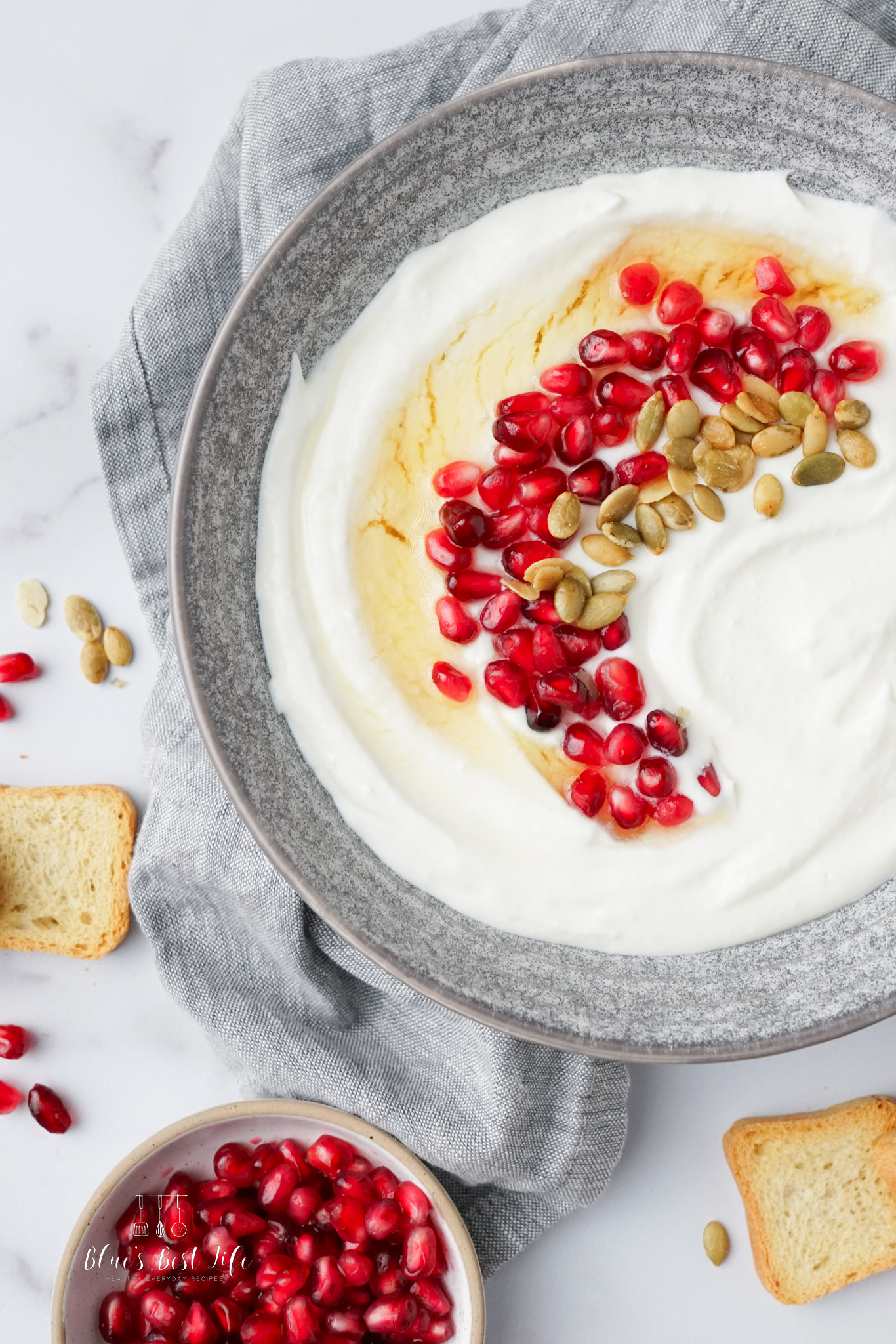 A serving bowl with whipped ricotta and honey drizzled.  Decorated with pomegranate arils and pepitas.  Small crostini for dipping.