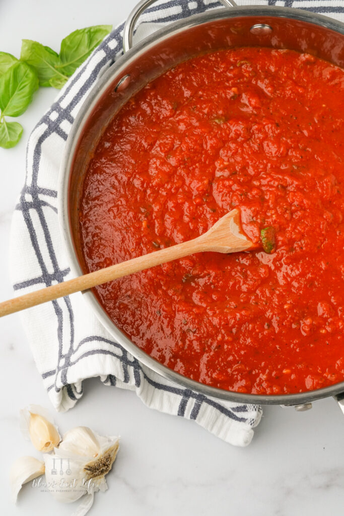 A sauce pan with spaghetti sauce and basil and garlic on the counter beside it.  