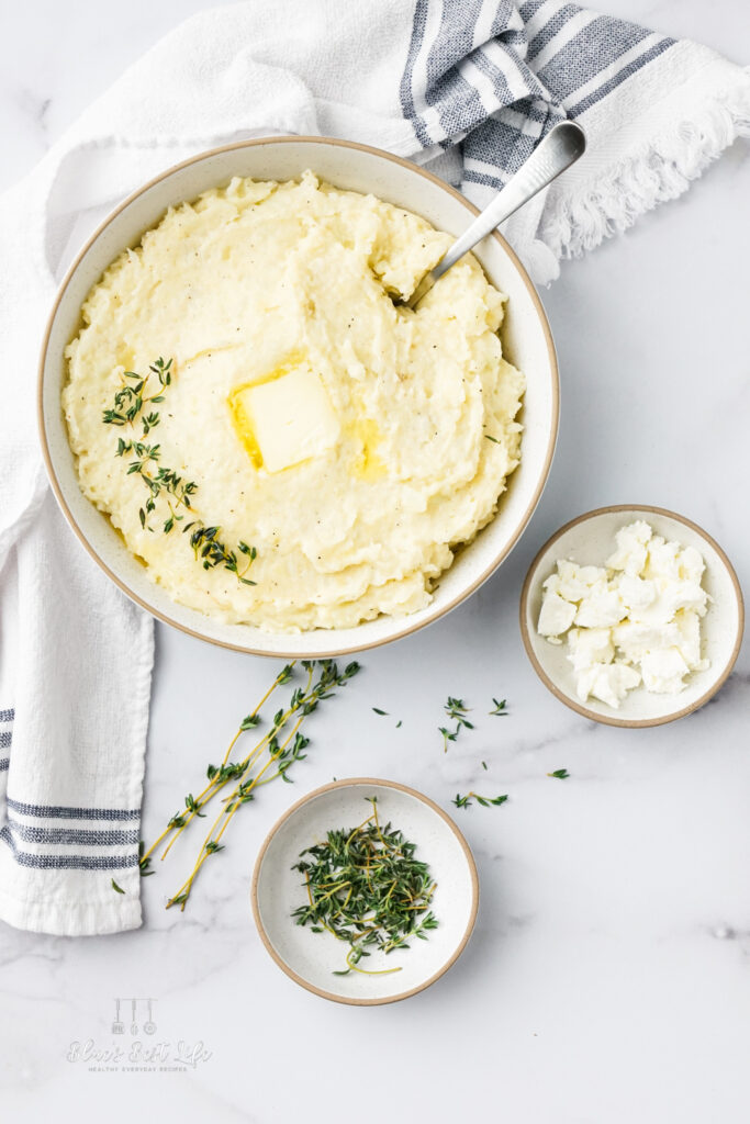 Potato and cauliflower mash in a serving bowl on a counter with a kitchen towel. 