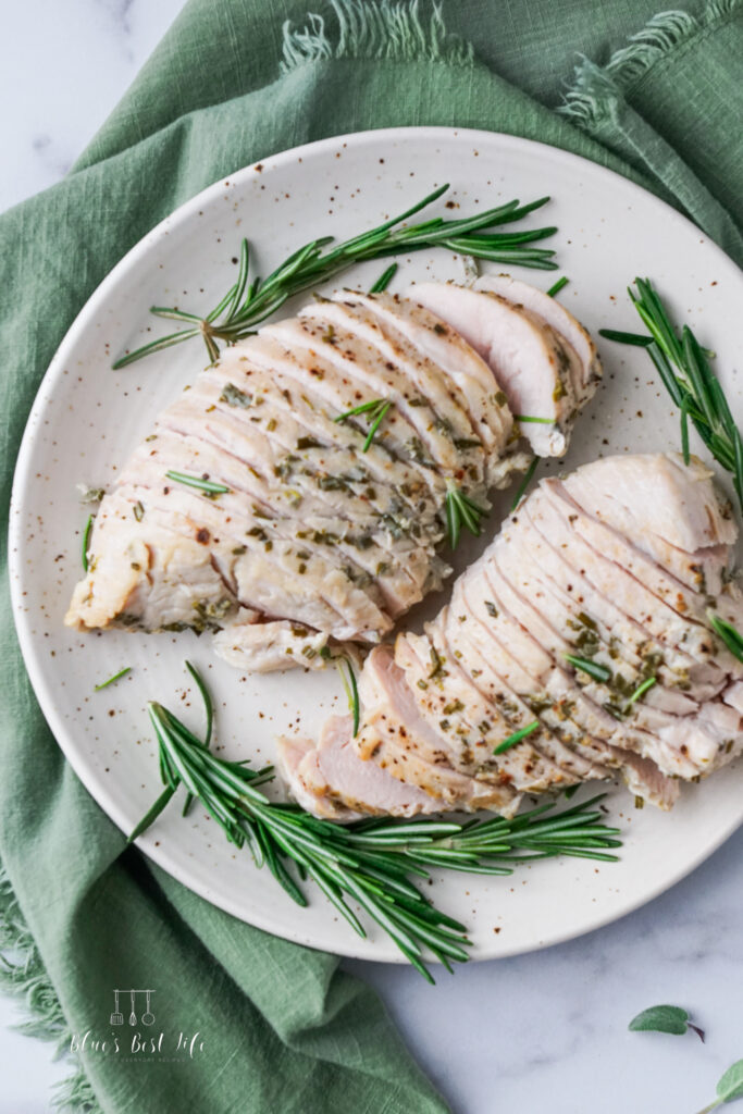 A picture of turkey tenderloin carved on a plate with fresh rosemary