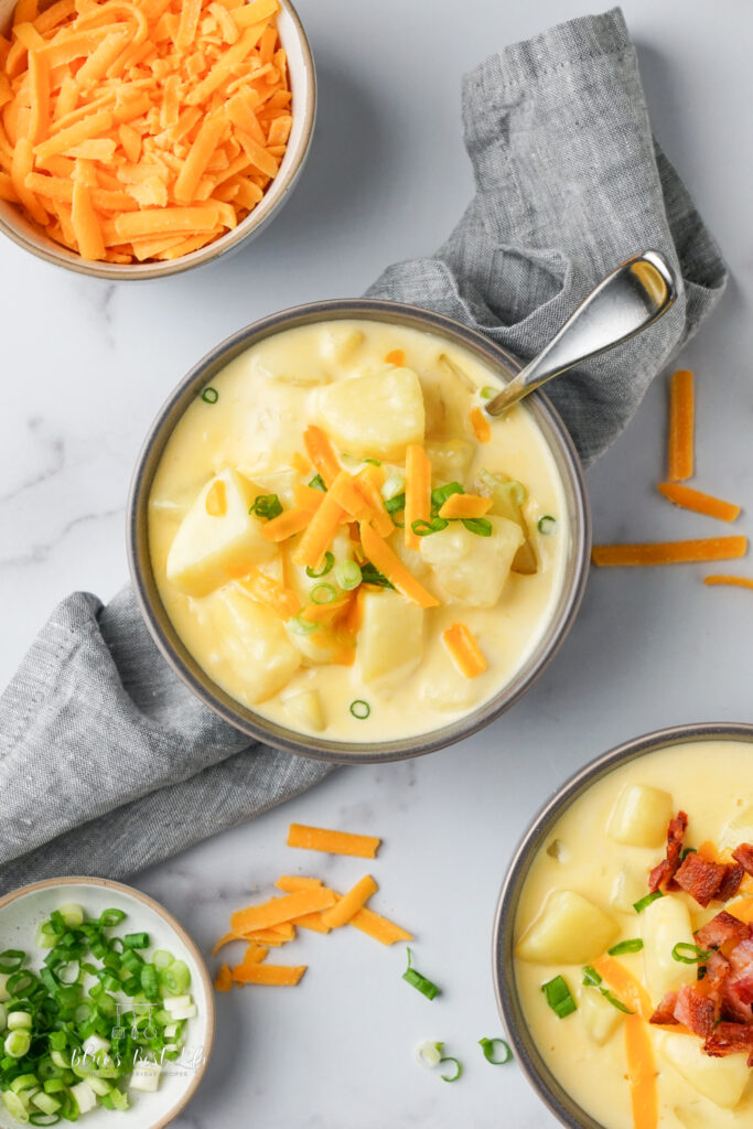 Bowls of potato soup with garnishes of bacon, green onions and shredded cheese. 
