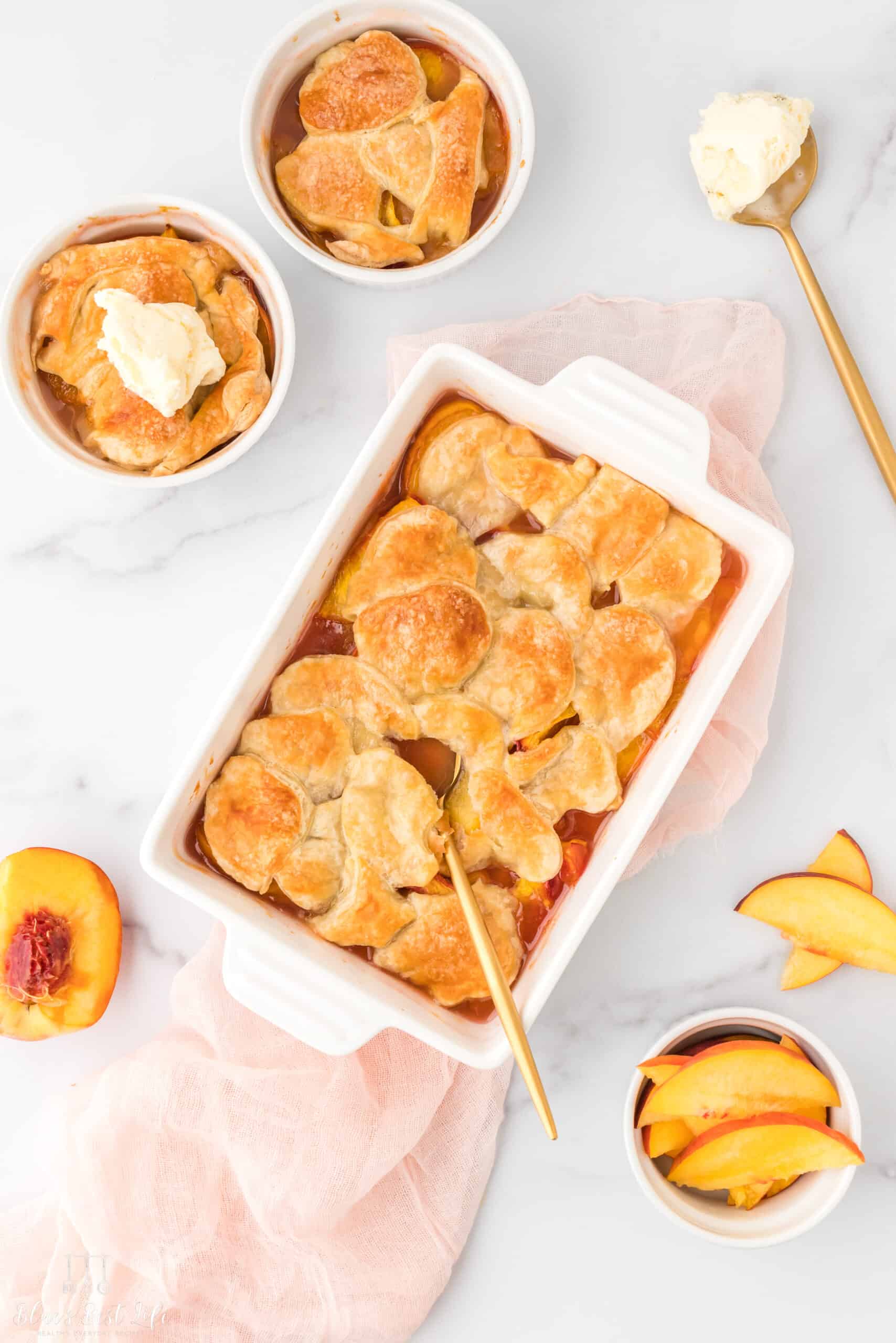 A peach cobbler in a baking dish plus individual serving cups with a scoop of ice cream. 