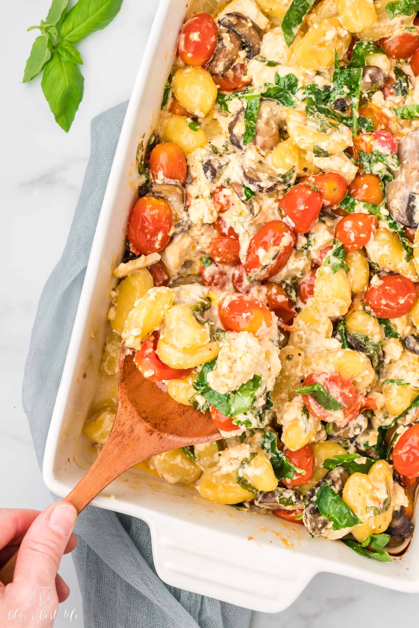 A baking dish with tomatoes, mushrooms, spinach and gnocchi with a creamy sauce.