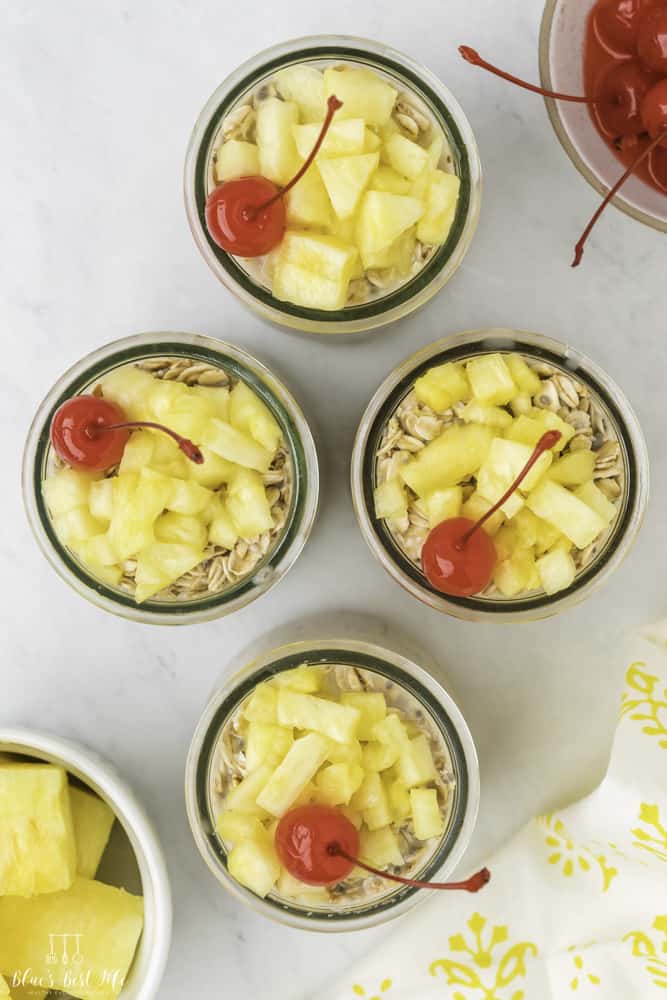 Top view of four clear glass with oats topped with pineapple and a cherry.