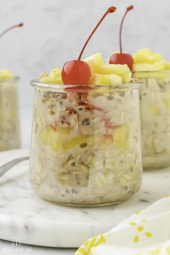 A jar of overnight oats with pineapple and a cherry. 