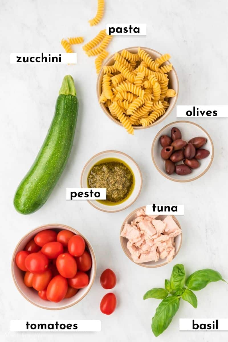 The ingredients to make pesto pasta with tuna.: pasta,. zucchini, pesto, olives, tuna, tomatoes, basil.