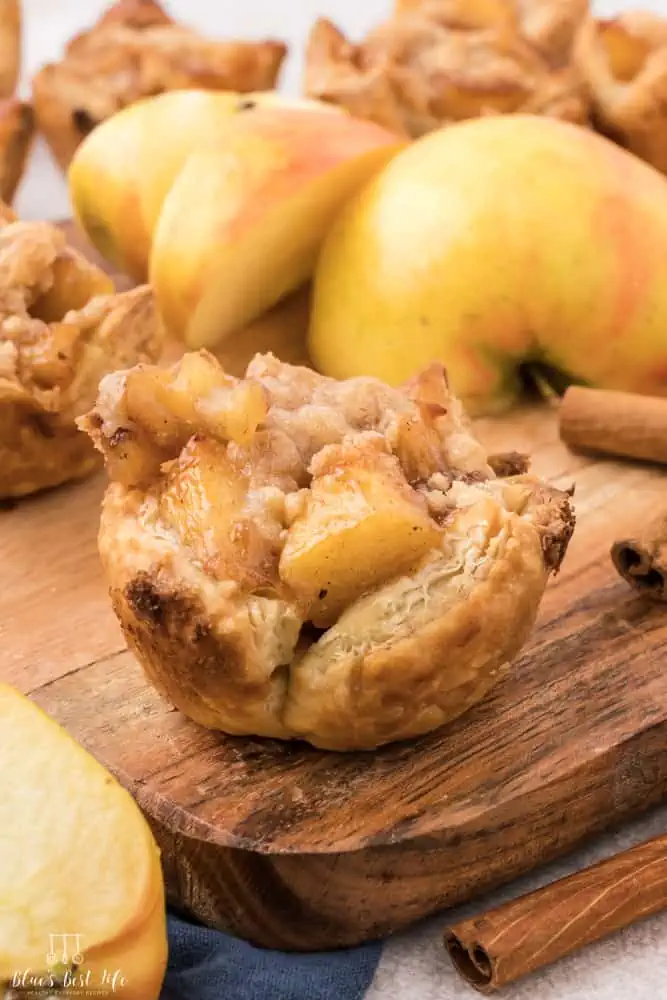 A mini apple pie on a cutting board with an apple. 