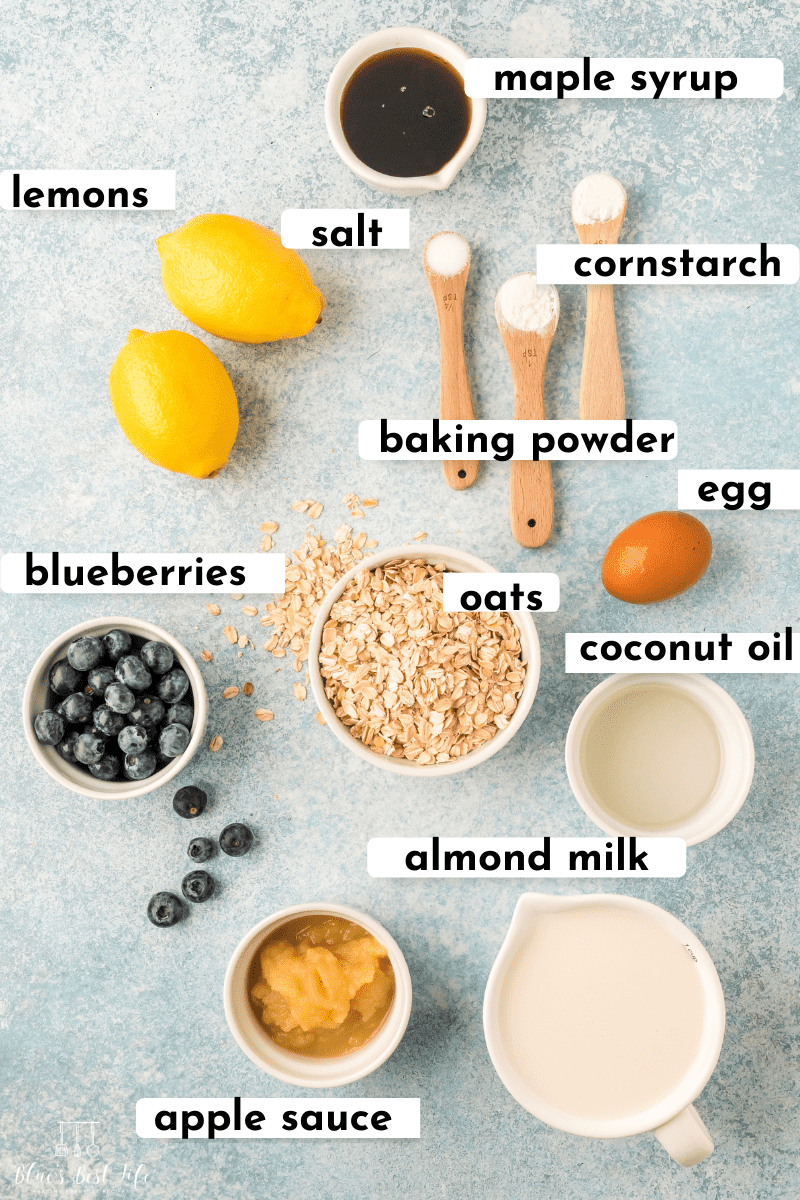 Flat lay of ingredients: maple syrup, lemons, salt, cornstarch, salt, baking soda, baking powder, egg, blueberries, oats, coconut oil, apple sauce, almond milk.