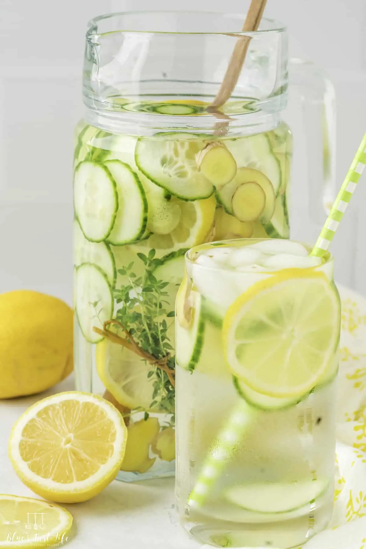 A glass with the pitcher of cucumber lemon ginger water. 