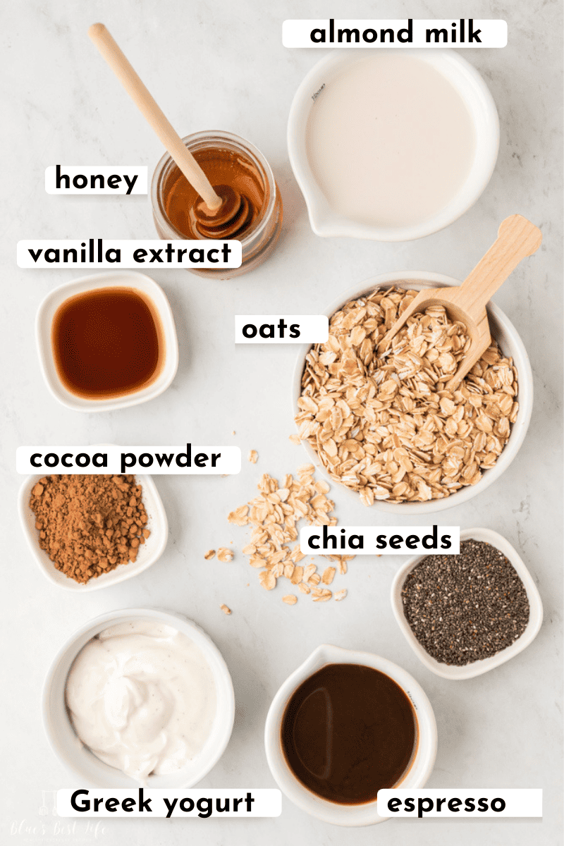 The ingredients needed for overnight oats: almond milk, honey, vanilla extract, oats, cocoa powder, chia seeds, Greek Yogurt, espresso. 
