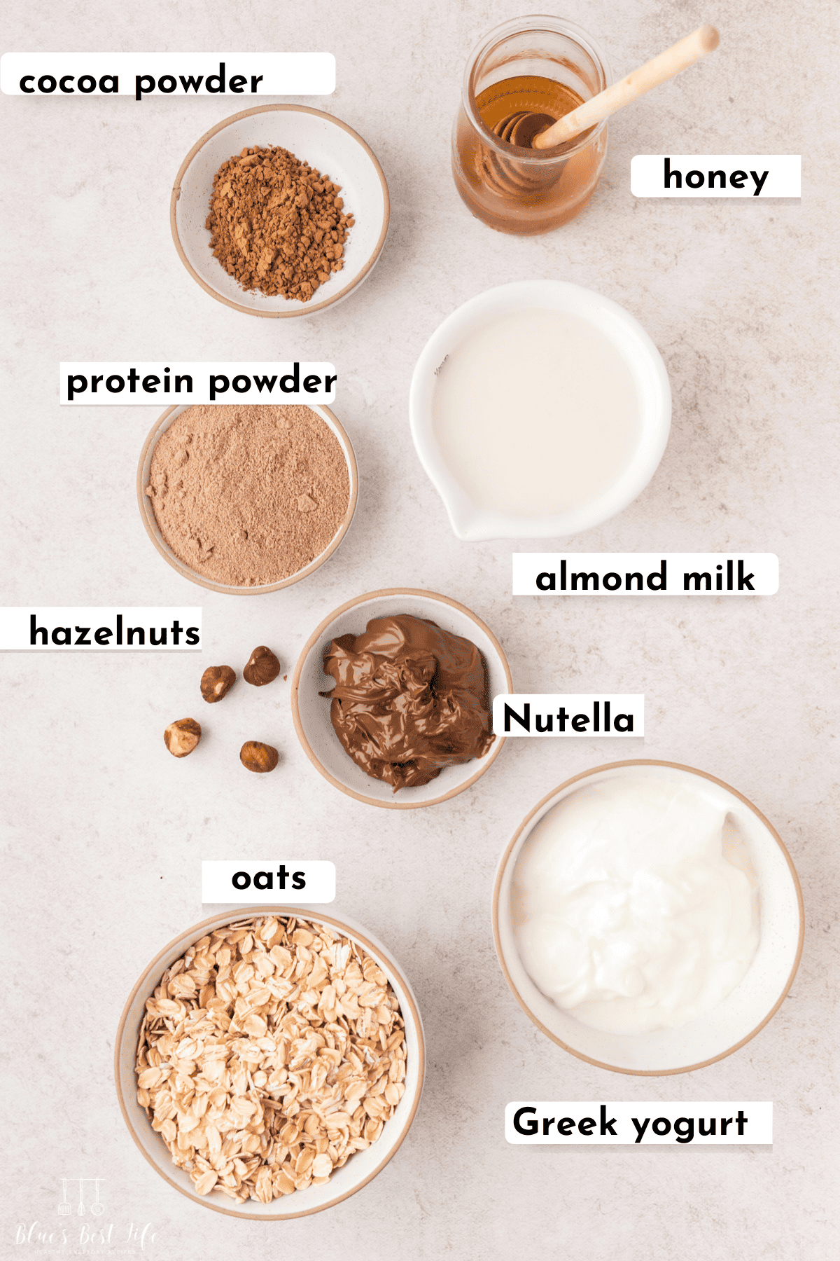 The ingredients for Nutella overnight oats: honey, cocoa powder, protein powder, hazelnuts, Nutella, almond milk, oats, & Greek Yogurt. 