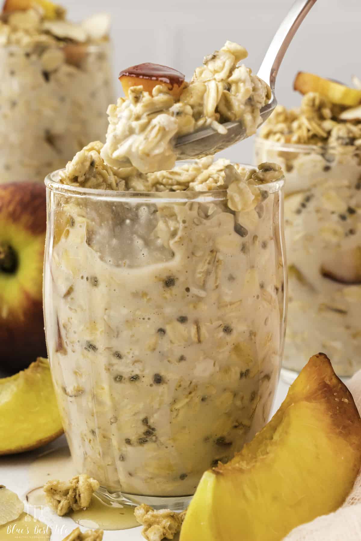 A spoonful of overnight peach oats from a single serving of overnight peach oats in a clear glass; other two servings visible in the background. 