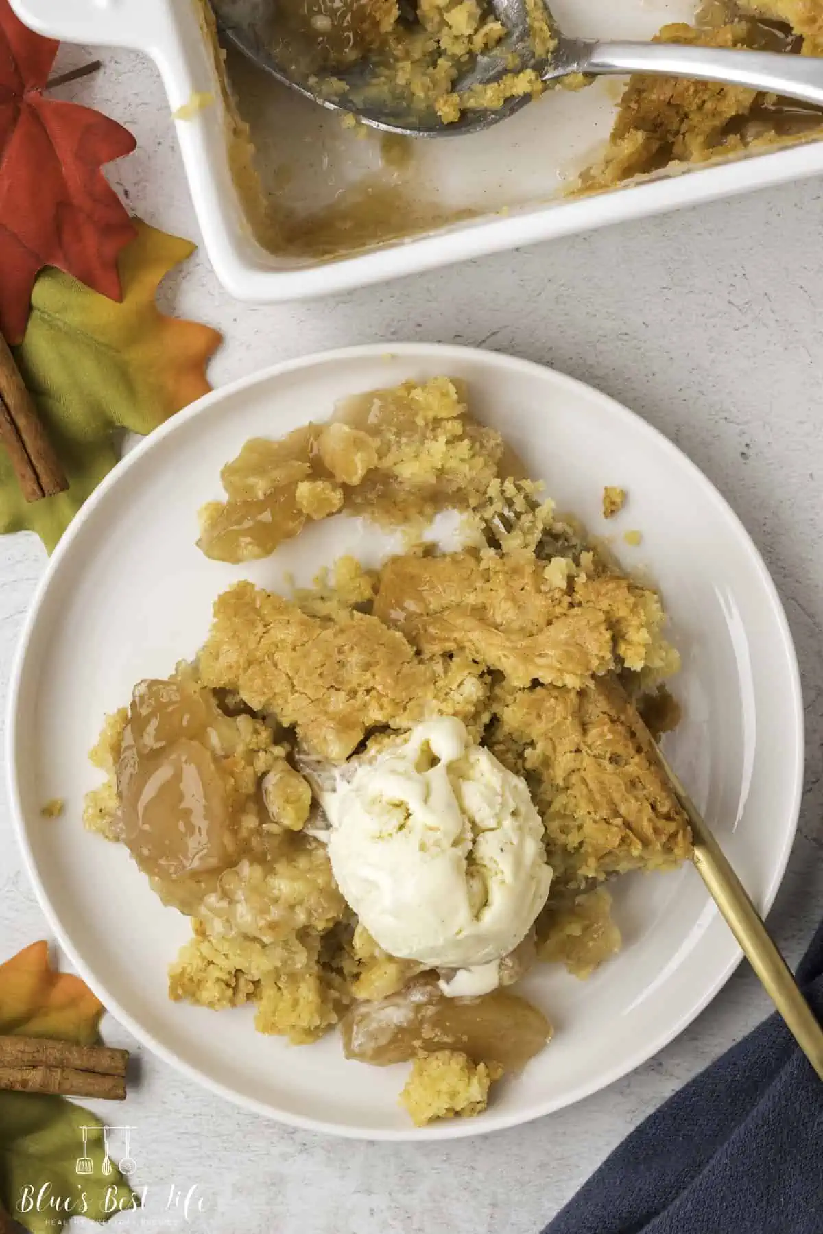 A piece of apple cobbler with cake mix on a plate with ice cream. 