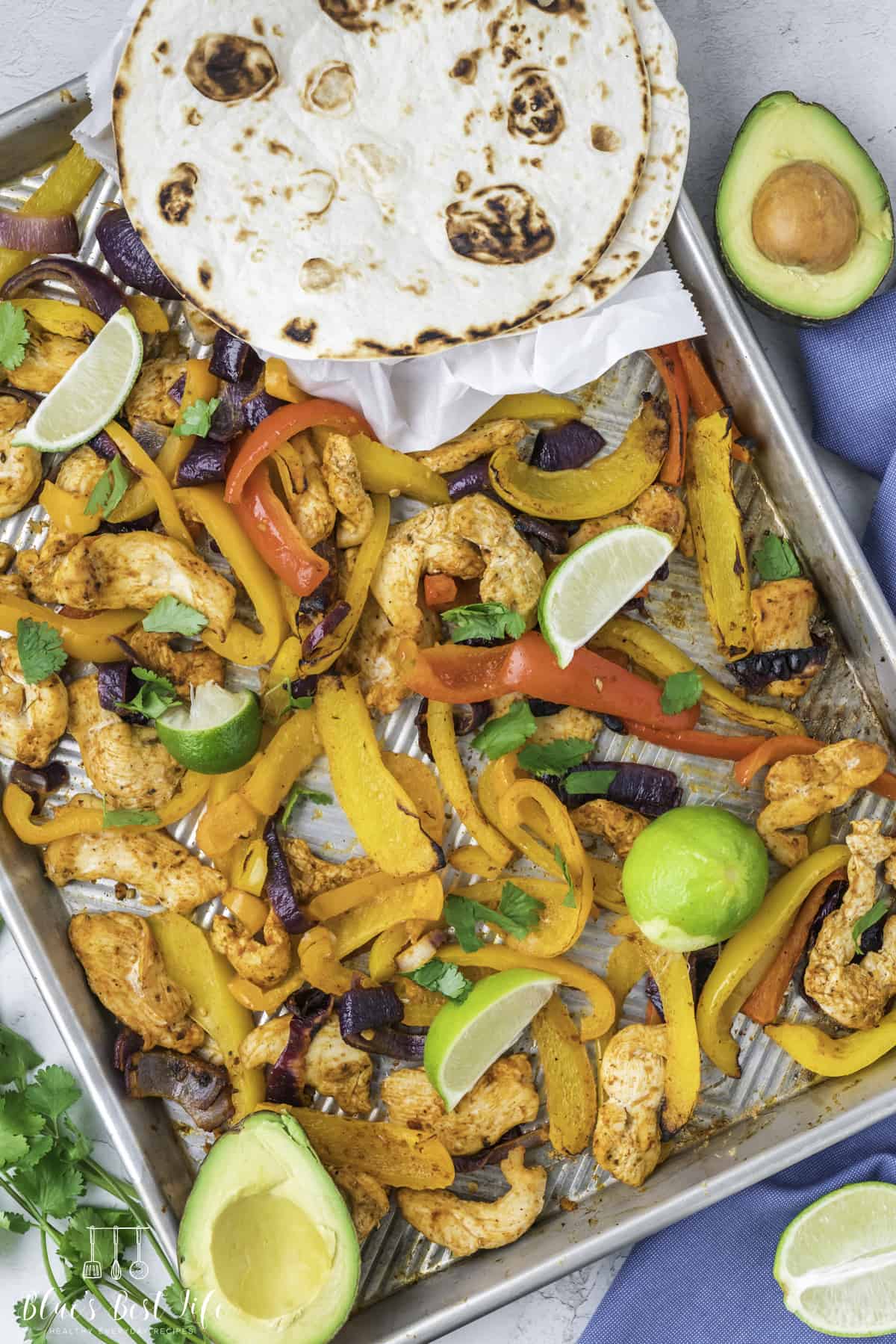 A sheet pan with chicken fajitas and tortillas. 