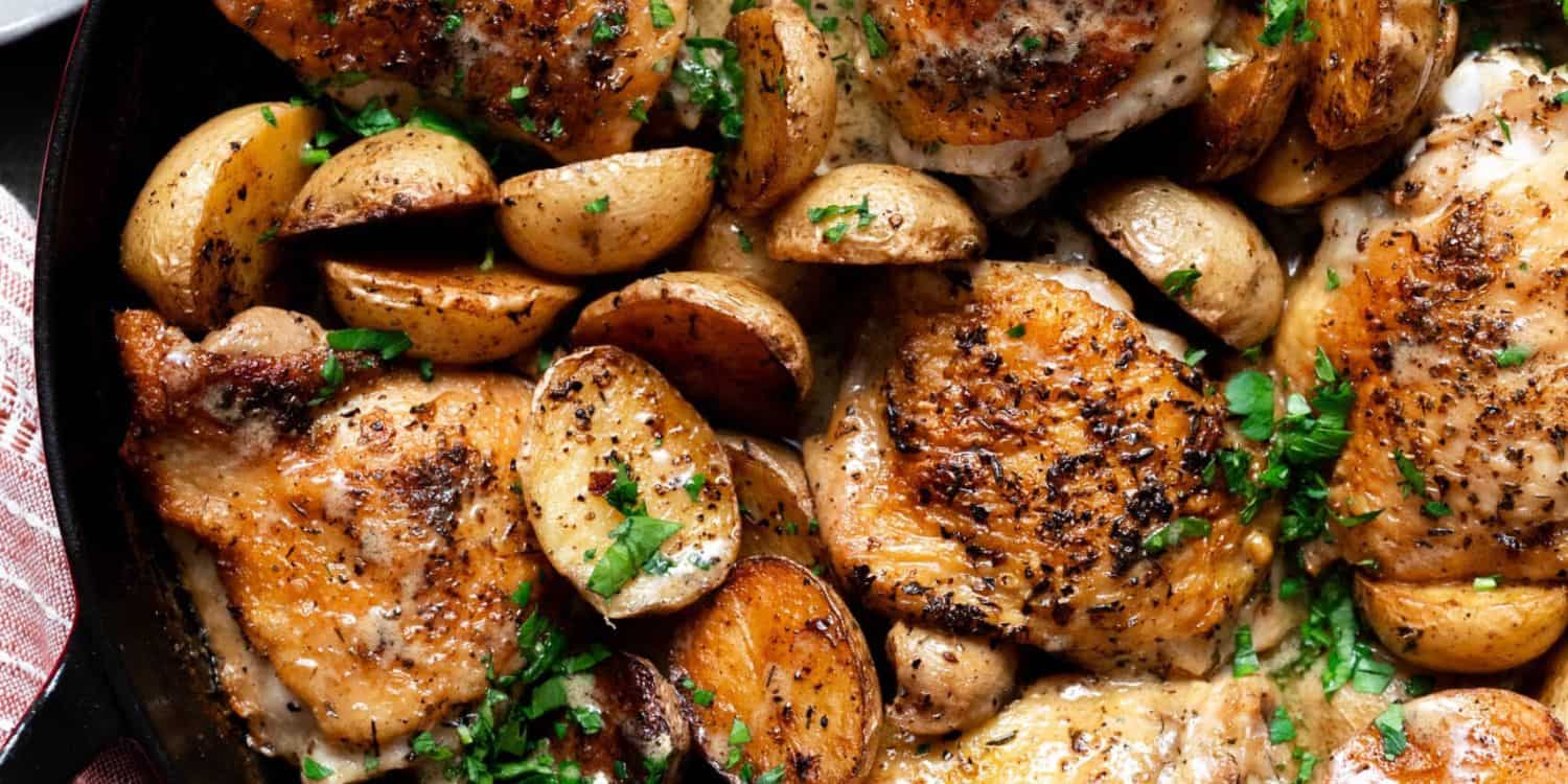 A close-up shot of Chicken Thighs and potato on a skillet. 