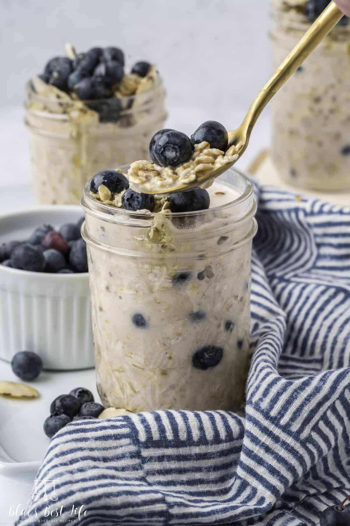 A spoonful of the blueberry overnight oats from a single serving in a glass mason jar; other servings is visible in the background.