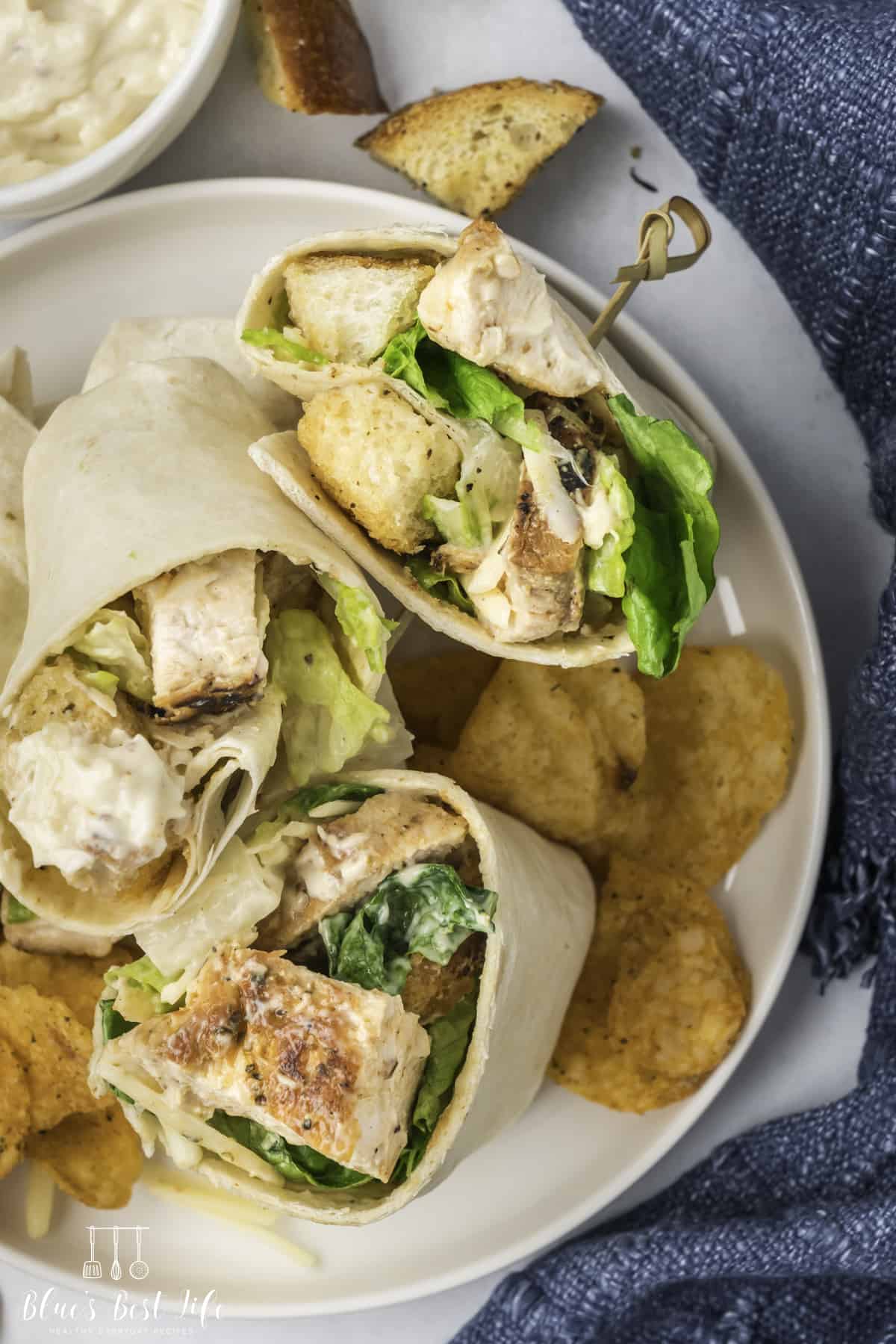 A top shot of Chicken Caesar Salad Wraps served on a plate with chips. 