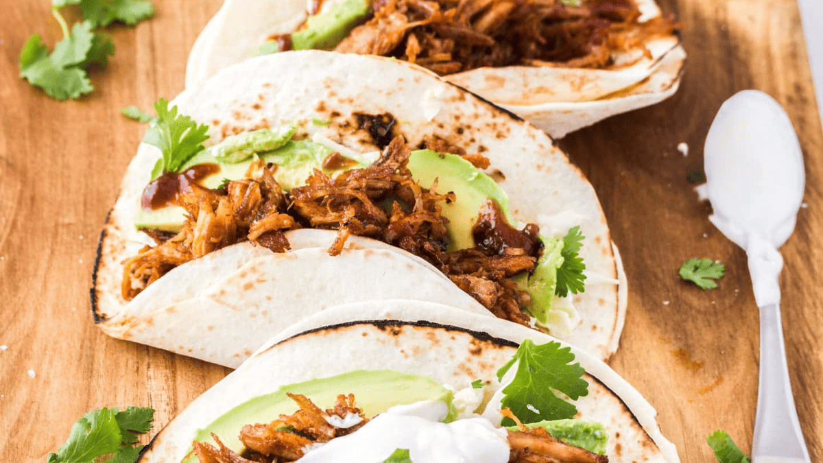 three tacos with pulled pork, avocado and cilantro