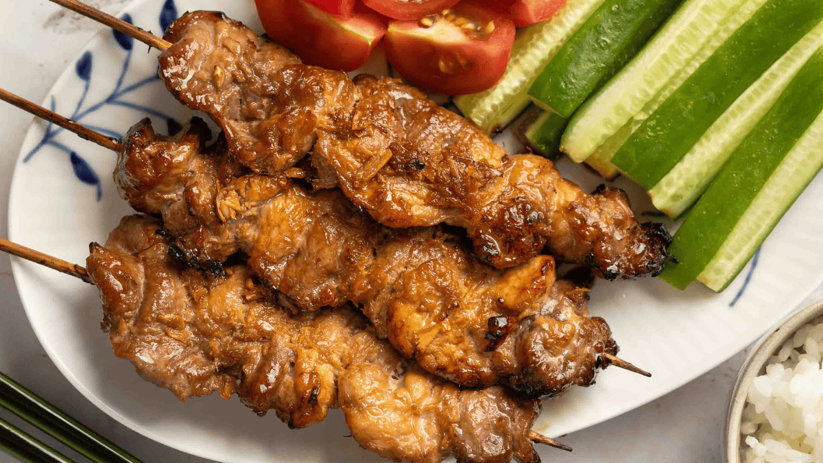 three pork skewers on a plate with sliced fresh tomatoes and cucumbers