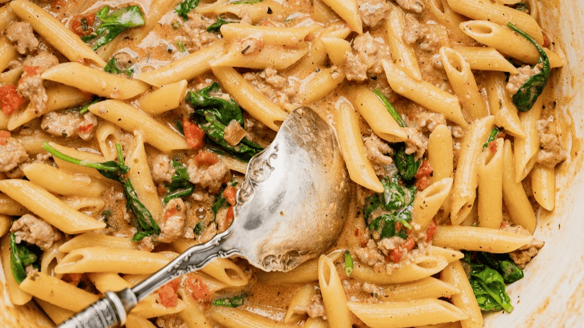 skillet full of pennes pasta with ground pork and spinach
