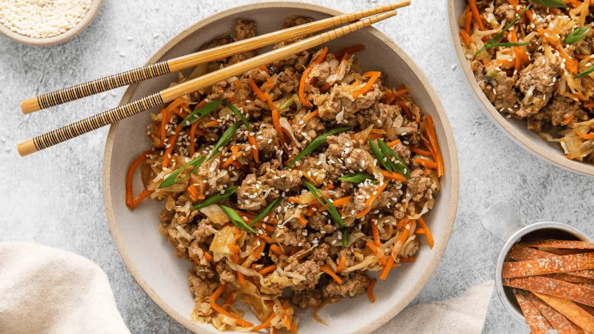 a bowl with ground pork, coleslaw mix, and chopstick on the side of the bowl