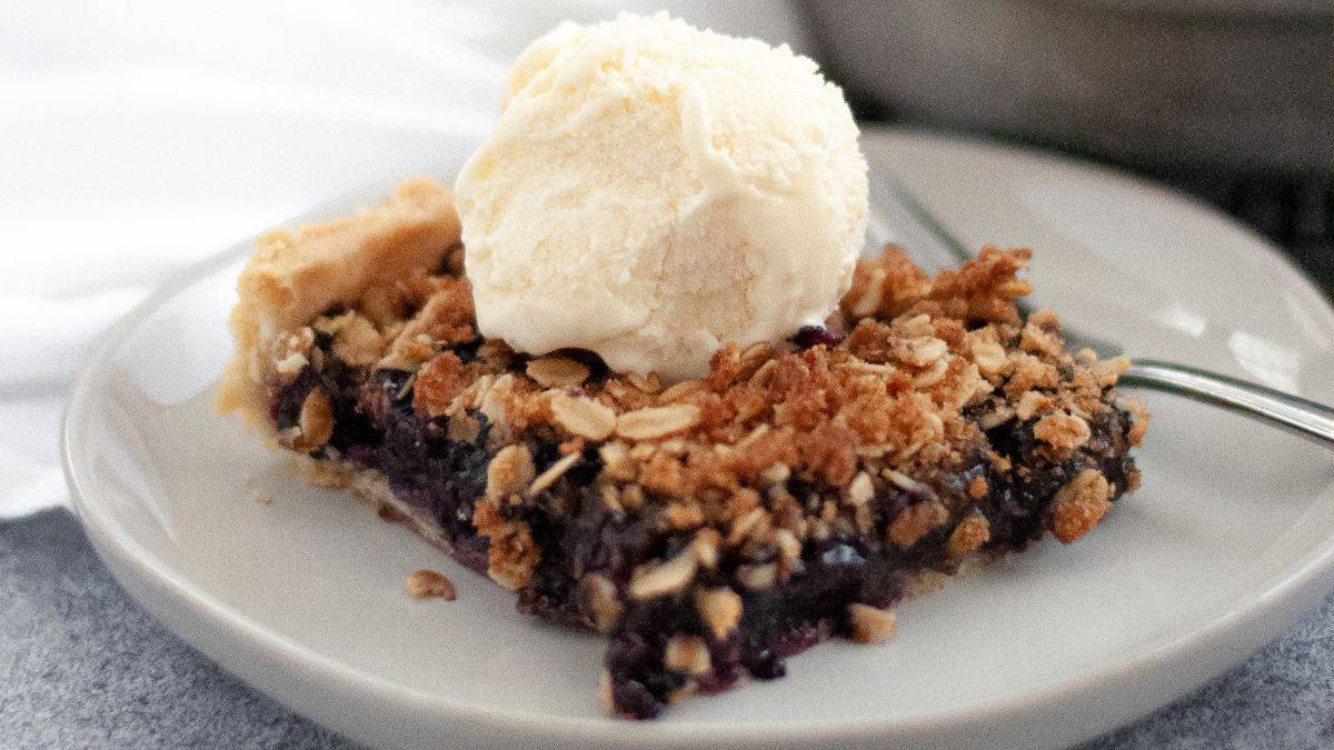 a square slice of blueberry orange crumble pie with vanilla ice cream on top