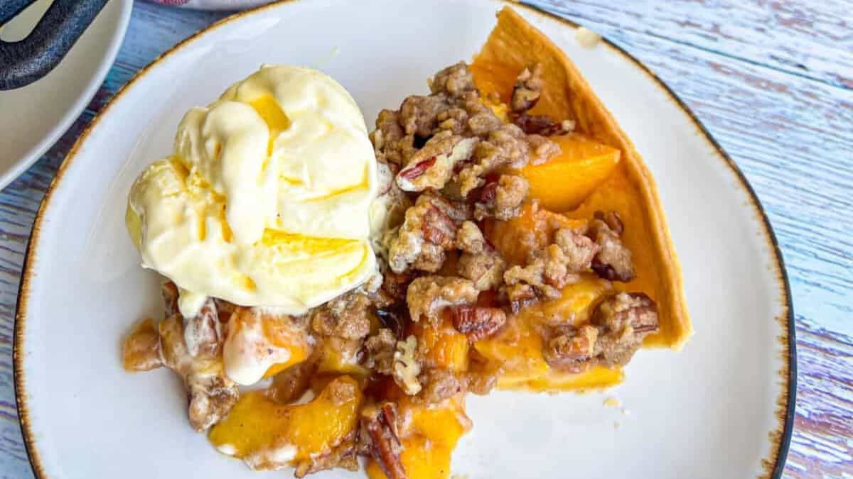 a slice of the peach crumb pie topped with brown sugar and pecans and served with vanilla ice cream