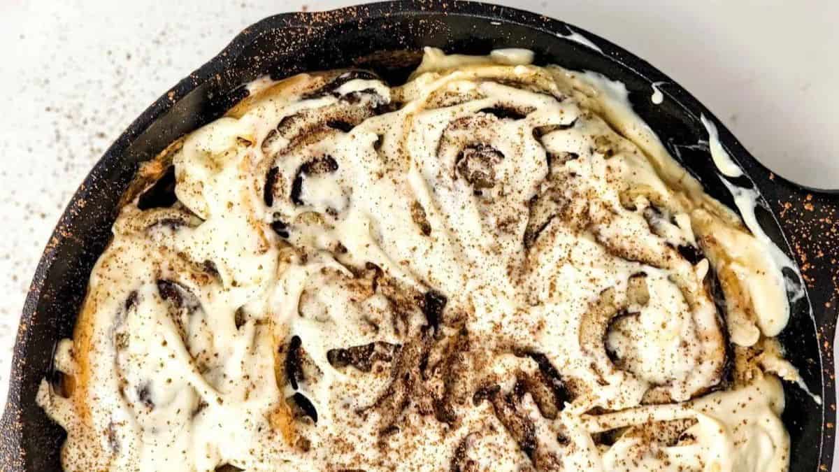 cast iron with cinnamon rolls topped with cream cheese frosting