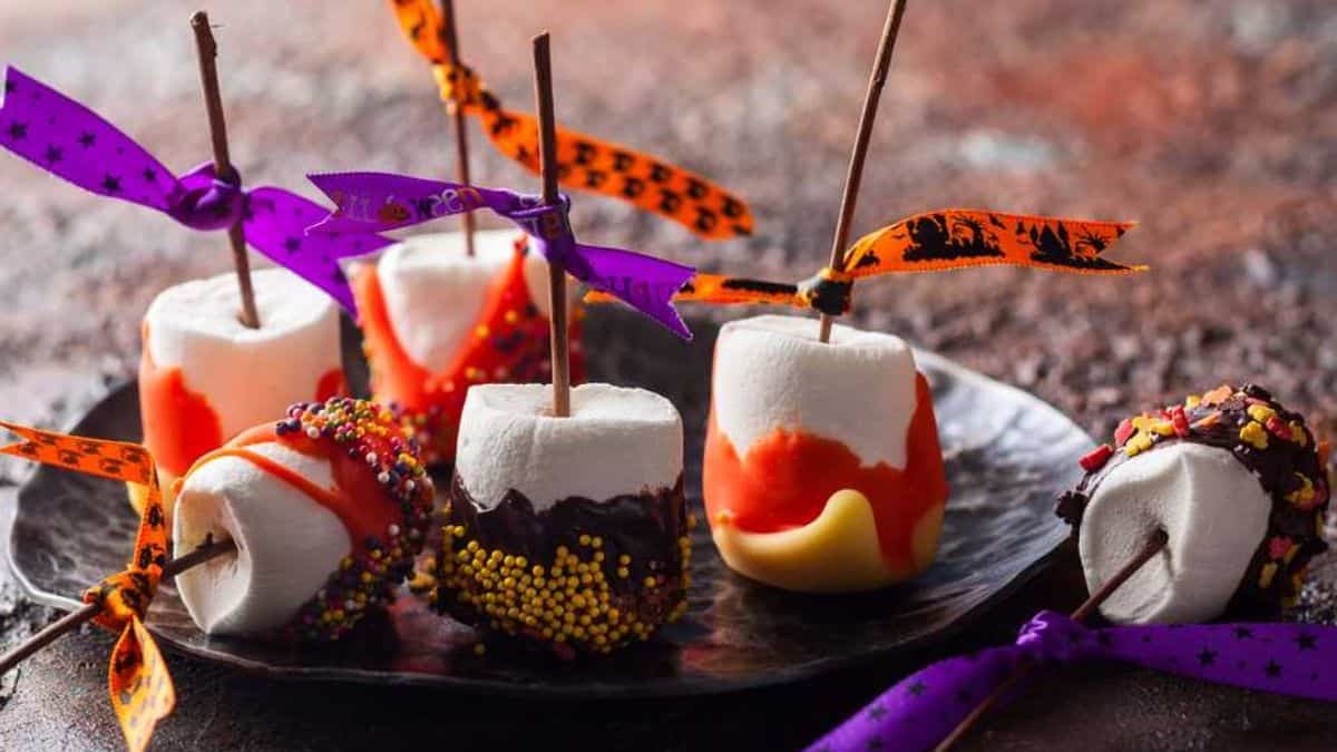 several marshmallows pops on sticks decorated with tinted orange or dark chocolate and rolled in sprinkles