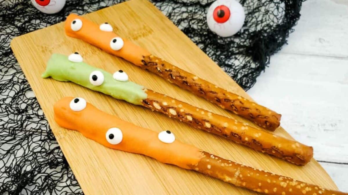 three pretzel rods covered in orange and green chocolate with googly eyes attached