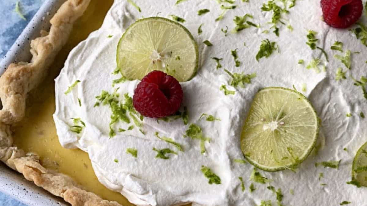 key lime slab pie in the sheet pan topped with frosting, raspberries, and lime slices