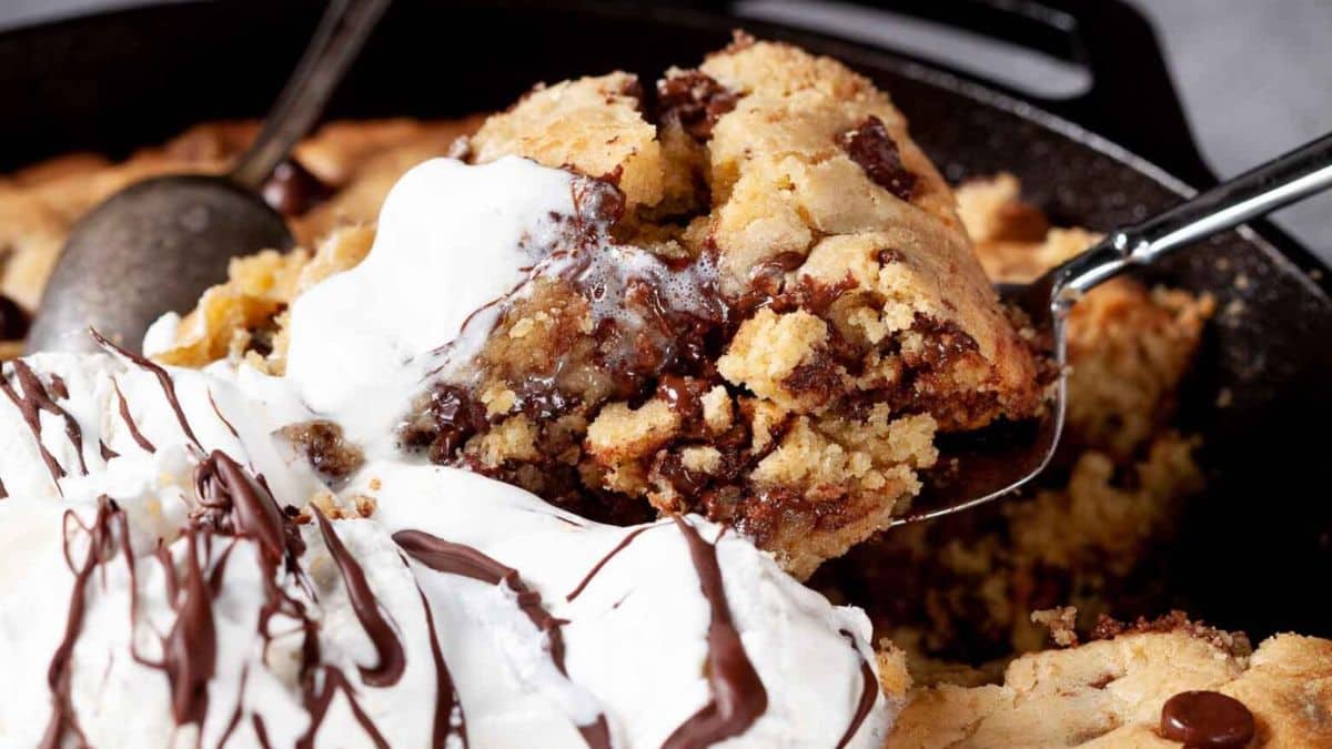 a skillet with thick chocolate chip cookie topped with vanilla ice cream and chocolate drizzle