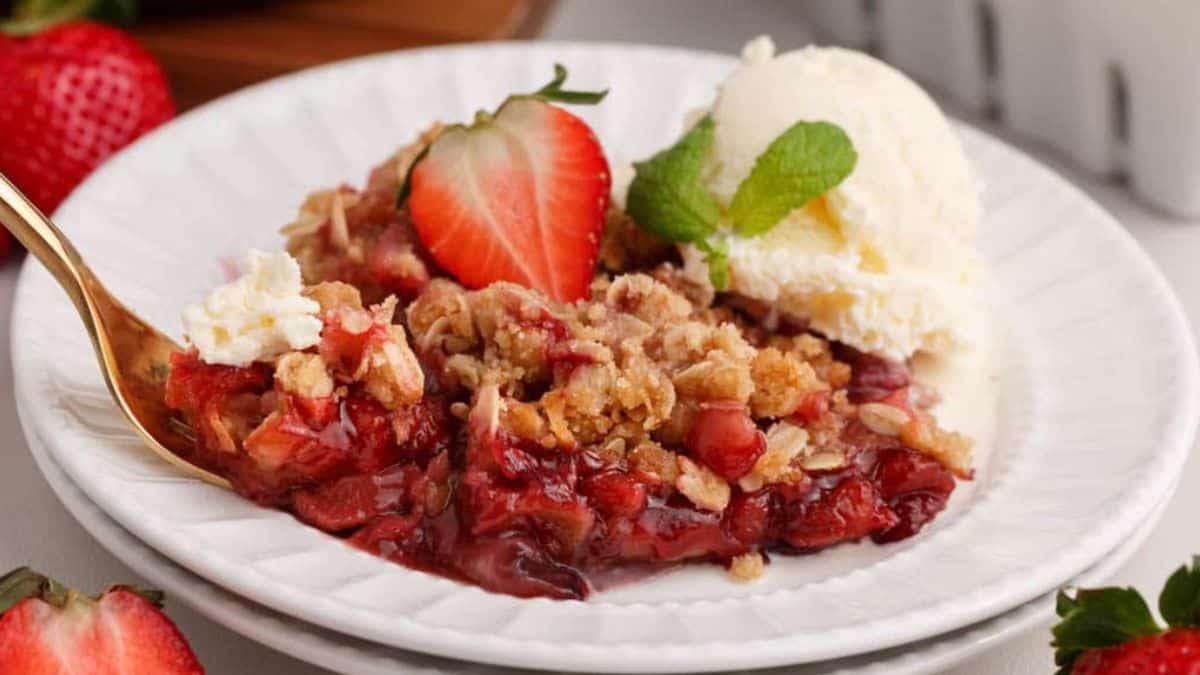 a portion of strawberry crisp served on a plate with fresh strawberry, mint, and vanilla ice cream