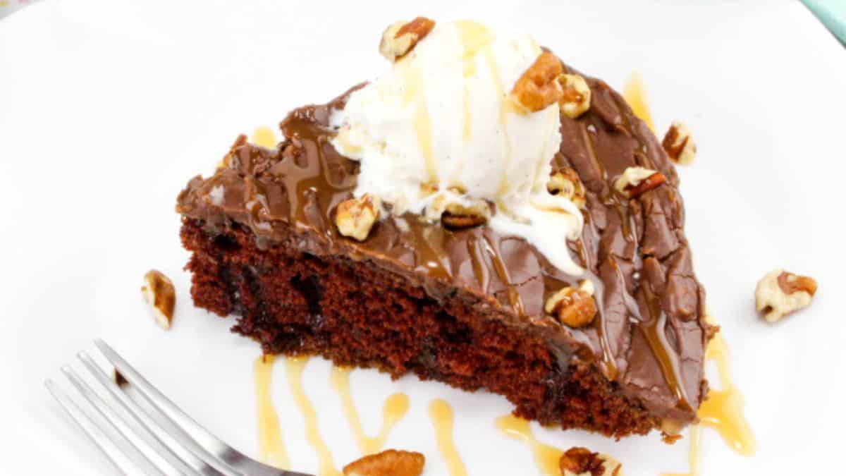 a slice of chocolate cake topped with chocolate ganache, nuts, and ice cream